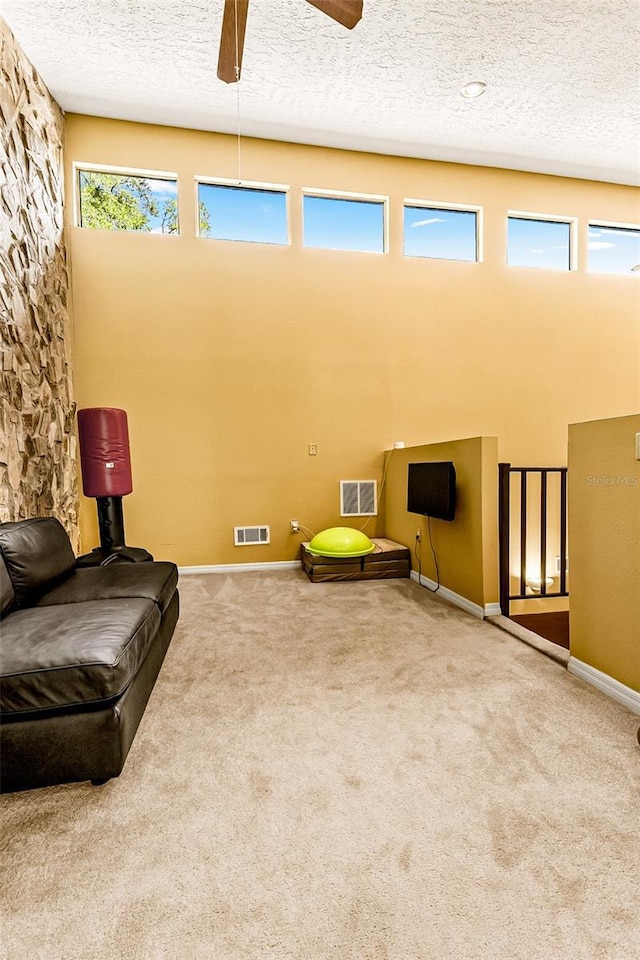 sitting room with ceiling fan, carpet, a towering ceiling, and a textured ceiling