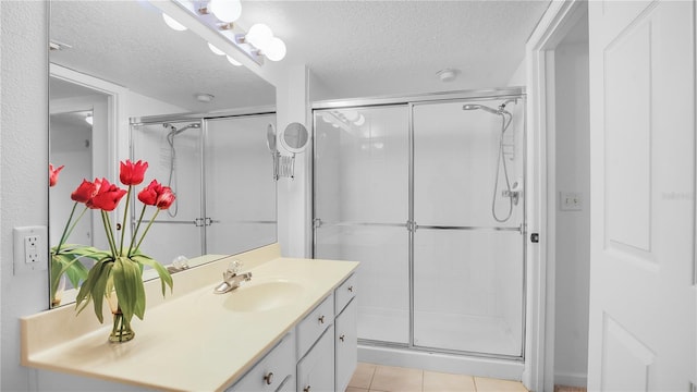 bathroom with a textured ceiling, walk in shower, vanity, and tile patterned flooring