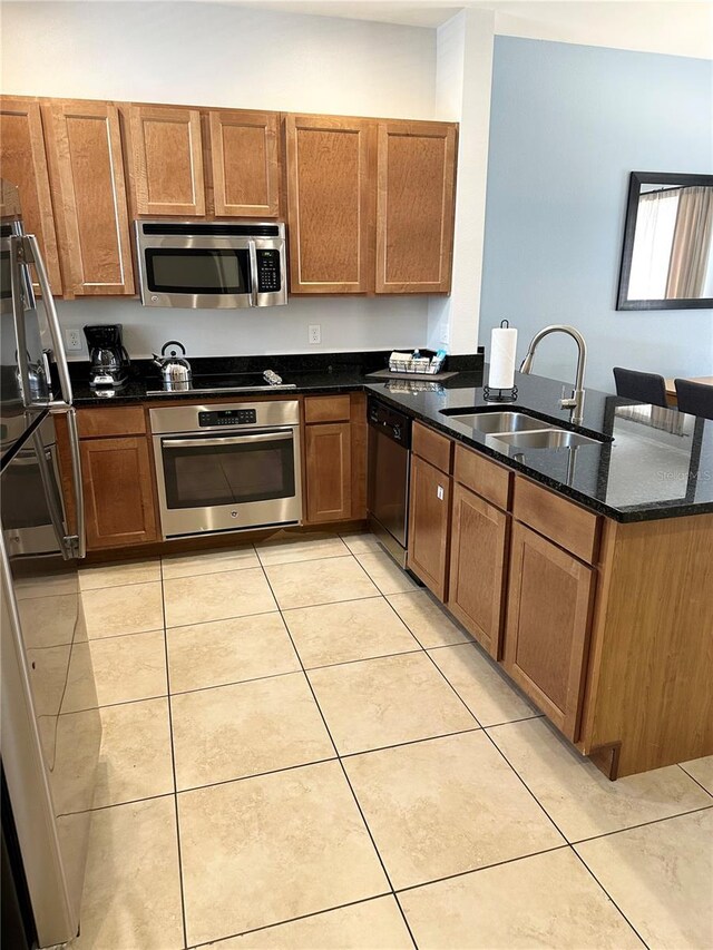 kitchen featuring dark stone counters, sink, light tile patterned floors, and stainless steel appliances