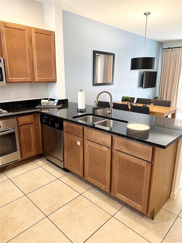 kitchen with kitchen peninsula, dark stone counters, stainless steel appliances, sink, and hanging light fixtures