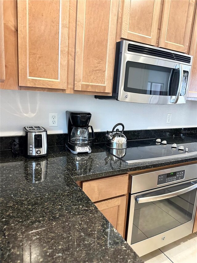 kitchen featuring tile patterned floors, dark stone countertops, and appliances with stainless steel finishes