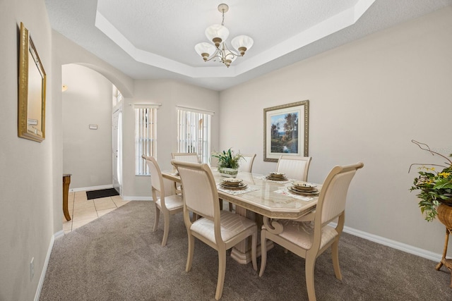 carpeted dining room with a raised ceiling, a textured ceiling, and an inviting chandelier