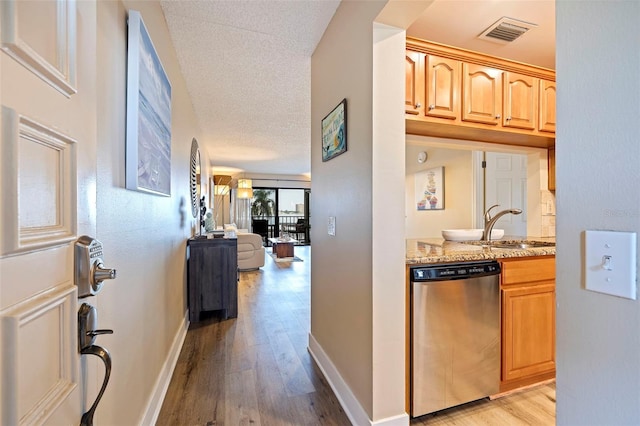 kitchen featuring light brown cabinetry, light stone counters, a textured ceiling, light wood-type flooring, and dishwasher