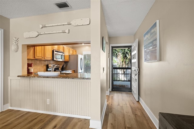 kitchen with stainless steel appliances, a textured ceiling, light hardwood / wood-style floors, and decorative backsplash