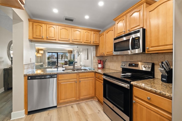 kitchen featuring sink, light stone counters, appliances with stainless steel finishes, light hardwood / wood-style floors, and backsplash