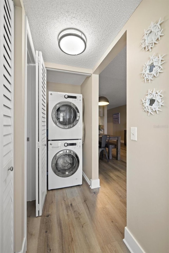 clothes washing area featuring stacked washer / dryer, a textured ceiling, and light hardwood / wood-style floors