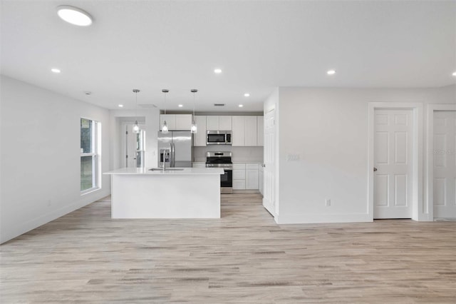 kitchen with appliances with stainless steel finishes, pendant lighting, white cabinetry, a kitchen island with sink, and light hardwood / wood-style floors