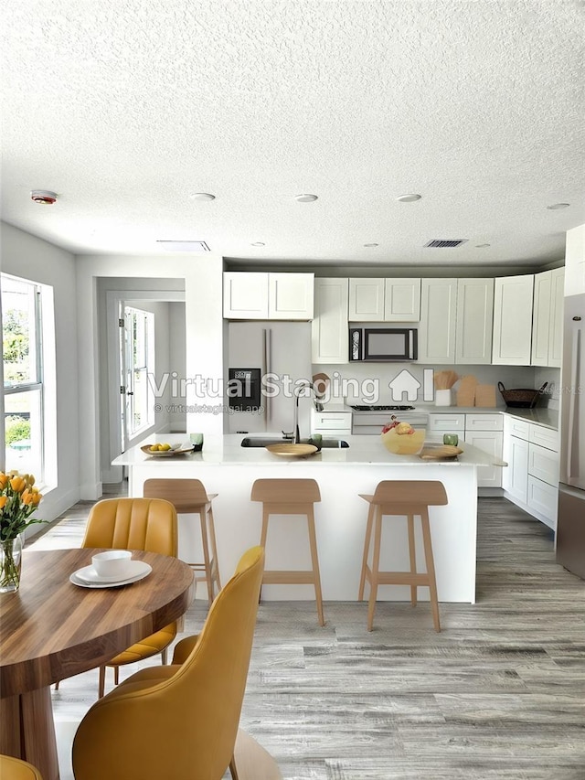 kitchen featuring stainless steel refrigerator with ice dispenser, stove, a breakfast bar, and white cabinets