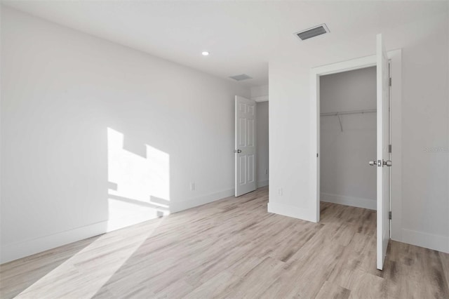 unfurnished bedroom with a spacious closet, a closet, and light wood-type flooring