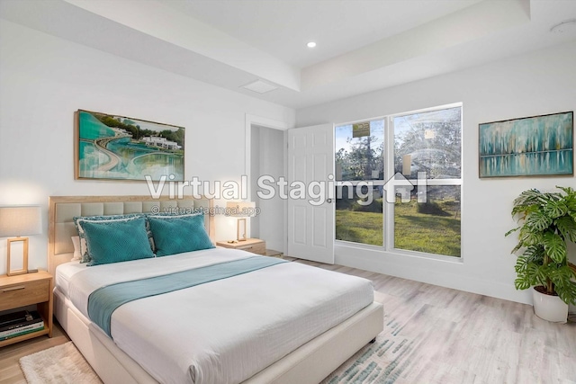 bedroom with light hardwood / wood-style floors and a raised ceiling