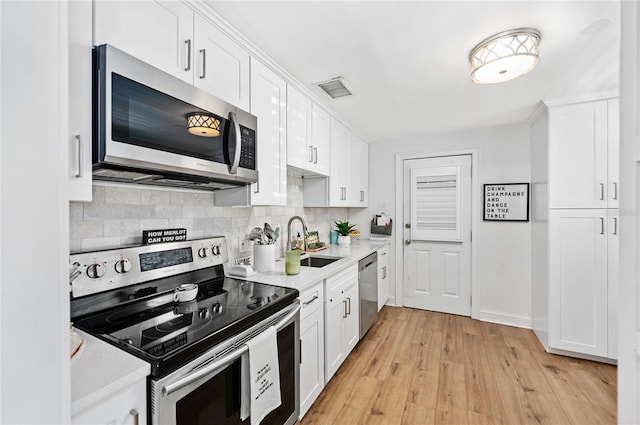 kitchen with white cabinetry, sink, tasteful backsplash, light hardwood / wood-style flooring, and appliances with stainless steel finishes