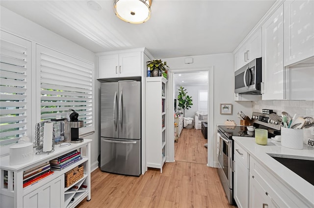 kitchen with white cabinets, sink, decorative backsplash, light wood-type flooring, and stainless steel appliances