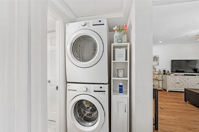 clothes washing area with hardwood / wood-style flooring and stacked washer and clothes dryer