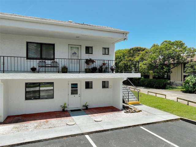 view of front facade featuring uncovered parking, stairway, and stucco siding