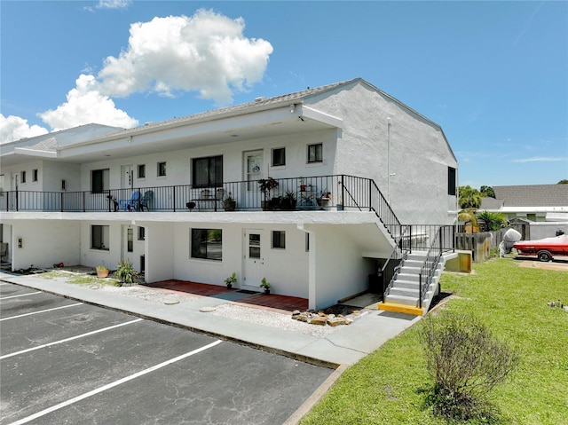 rear view of house with a balcony, a yard, stairway, stucco siding, and uncovered parking