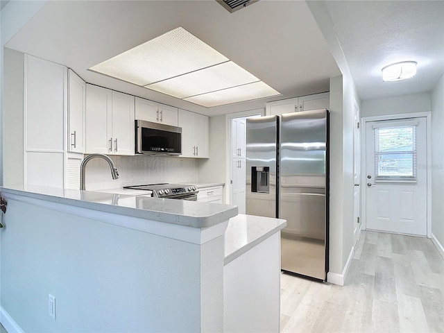 kitchen with light wood-type flooring, kitchen peninsula, white cabinets, stainless steel appliances, and decorative backsplash