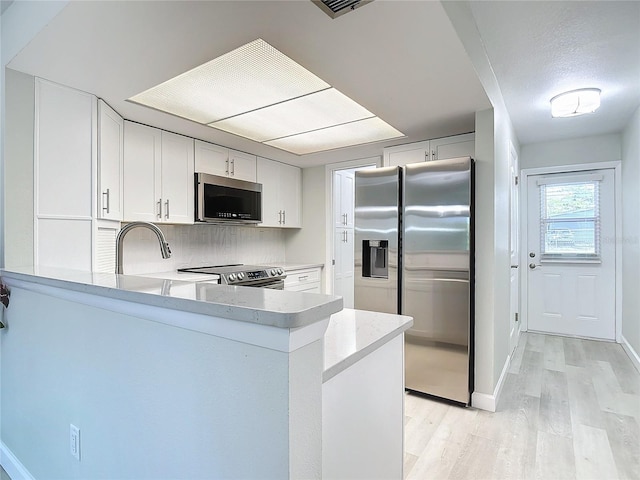 kitchen featuring light wood-style flooring, stainless steel appliances, a peninsula, white cabinetry, and light countertops