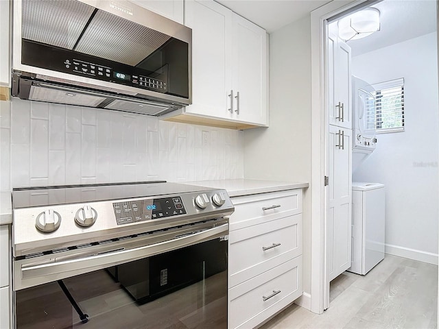 kitchen with white cabinetry, light countertops, appliances with stainless steel finishes, stacked washing maching and dryer, and backsplash