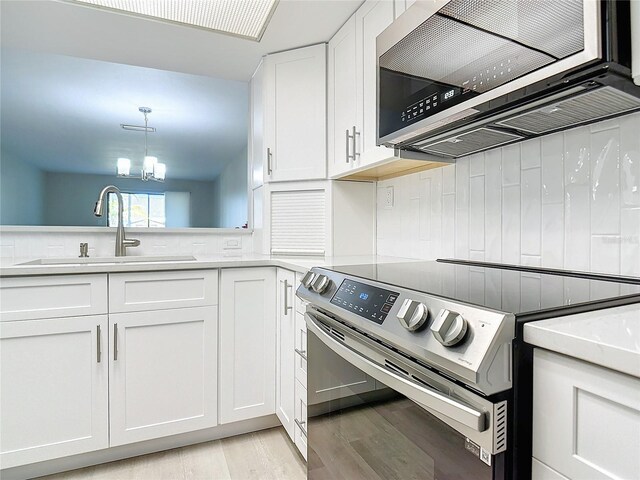 kitchen featuring a notable chandelier, stainless steel appliances, white cabinets, sink, and light hardwood / wood-style floors