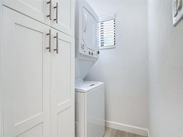 laundry area with cabinet space, baseboards, light wood-style floors, and stacked washer / drying machine