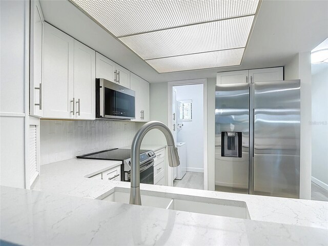 kitchen with white cabinetry, tasteful backsplash, appliances with stainless steel finishes, and light stone countertops