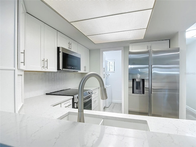 kitchen with light stone counters, backsplash, appliances with stainless steel finishes, white cabinets, and a sink