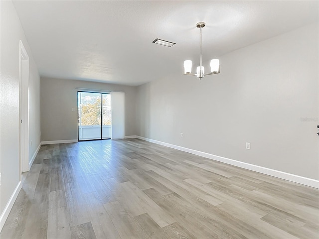 unfurnished room featuring baseboards, light wood finished floors, visible vents, and a notable chandelier