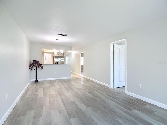 unfurnished living room featuring baseboards, an inviting chandelier, visible vents, and light wood-style floors