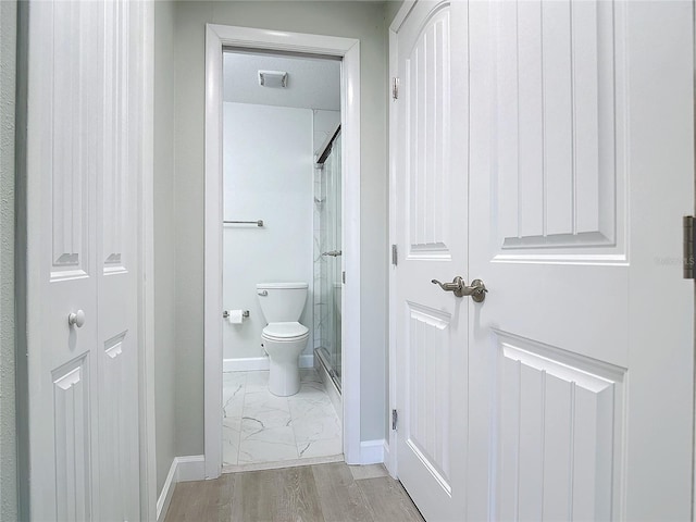 bathroom with a closet, toilet, a shower stall, wood finished floors, and baseboards