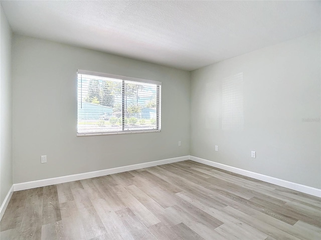 empty room featuring light wood finished floors, baseboards, and a textured ceiling