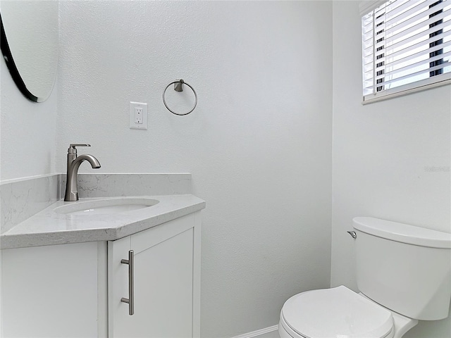 half bath featuring toilet, vanity, and baseboards