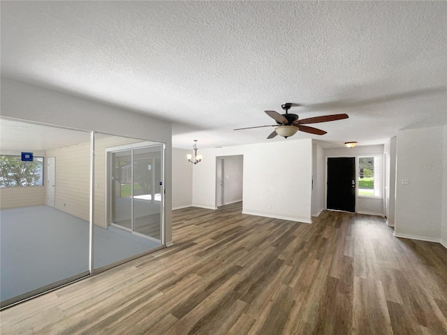 unfurnished living room featuring ceiling fan with notable chandelier, dark wood-type flooring, and a textured ceiling