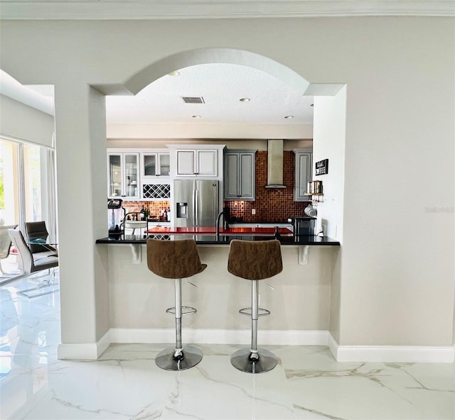 9060 Heritage Bay Cir, Orlando, FL 32836 - kitchen featuring wall chimney range hood, marble finish floor, stainless steel fridge, and arched walkways