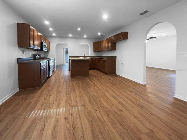 kitchen with light wood-type flooring, ceiling fan, sink, a center island with sink, and stainless steel range oven