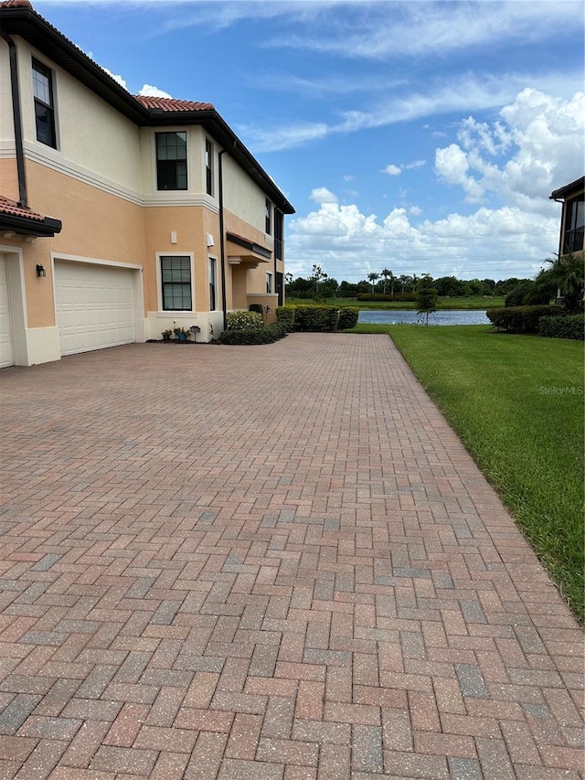 exterior space featuring a garage, decorative driveway, a water view, and stucco siding