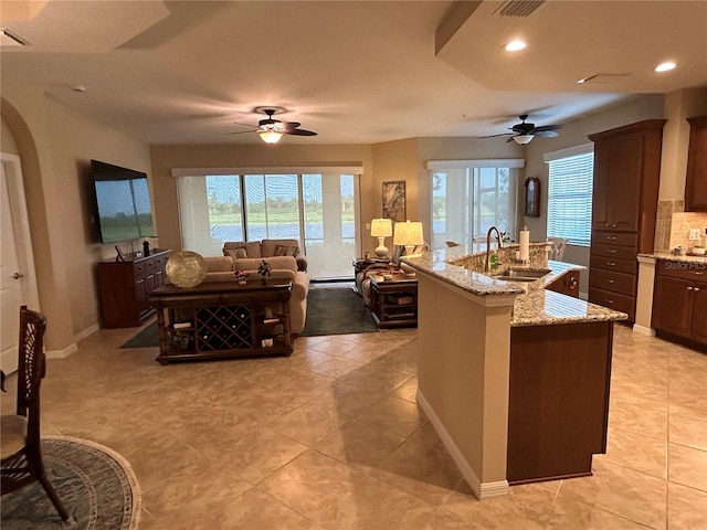 kitchen featuring arched walkways, light stone counters, a sink, tasteful backsplash, and an island with sink