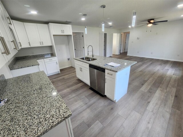 kitchen featuring stainless steel dishwasher, light hardwood / wood-style flooring, light stone counters, sink, and a center island with sink