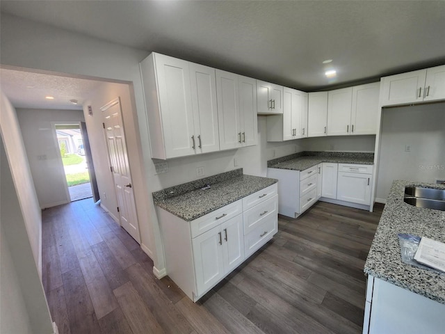 kitchen with stone counters, white cabinetry, baseboards, and dark wood-style flooring