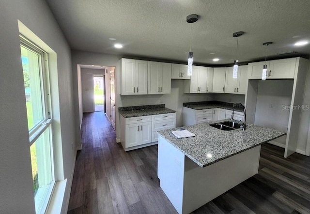 kitchen with light stone counters, white cabinetry, dark wood-type flooring, and a sink