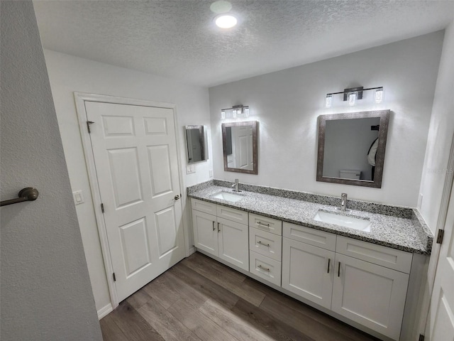 bathroom with a sink, a textured ceiling, wood finished floors, and double vanity