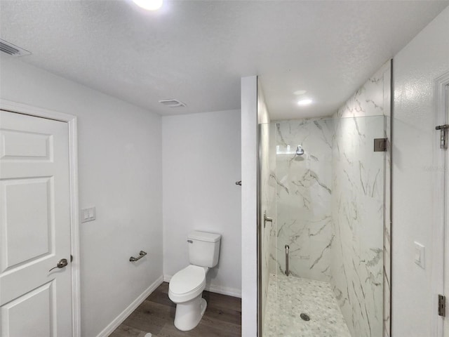 bathroom with toilet, a textured ceiling, a tile shower, and wood-type flooring