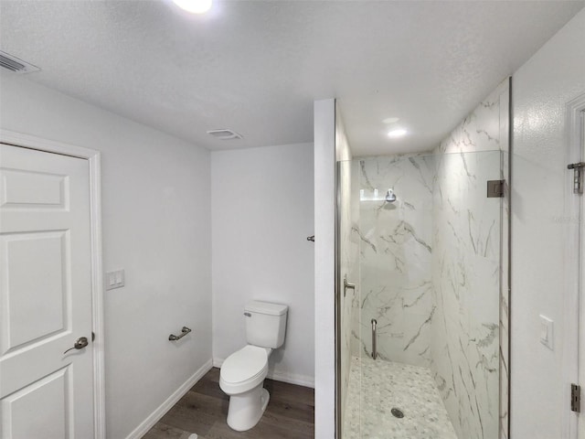 bathroom featuring wood finished floors, visible vents, baseboards, a marble finish shower, and toilet