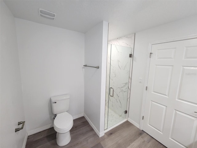 bathroom with wood-type flooring, a shower with shower door, and toilet