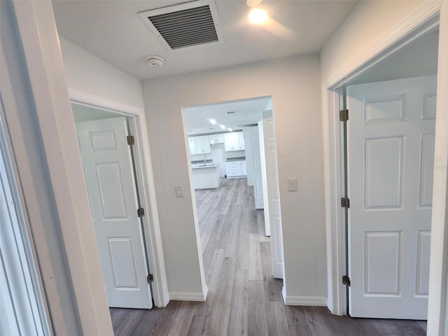 hall with visible vents, baseboards, and wood finished floors