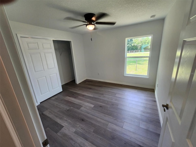 unfurnished bedroom with baseboards, a closet, a textured ceiling, a ceiling fan, and dark wood-style flooring