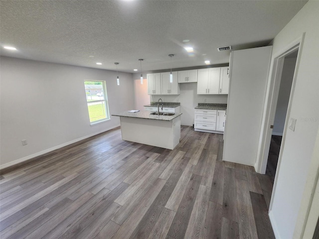 kitchen with hanging light fixtures, wood-type flooring, white cabinets, a textured ceiling, and a center island with sink