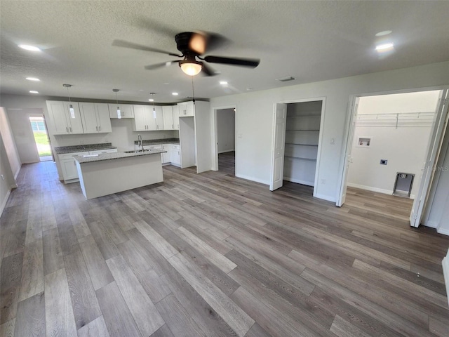 kitchen featuring a ceiling fan, wood finished floors, a center island with sink, a sink, and white cabinetry