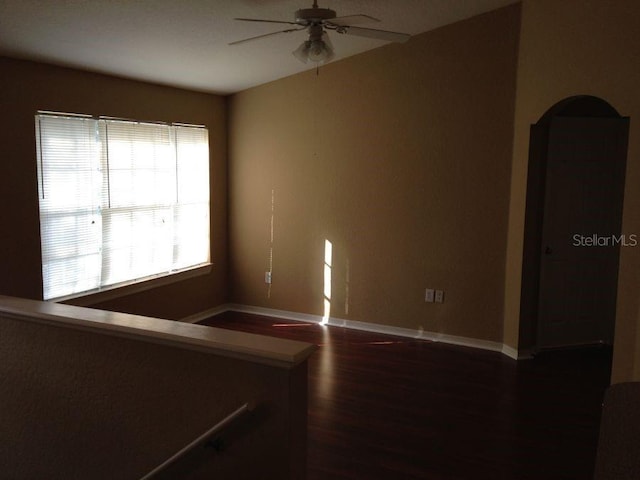 empty room with dark wood-type flooring, baseboards, and a ceiling fan