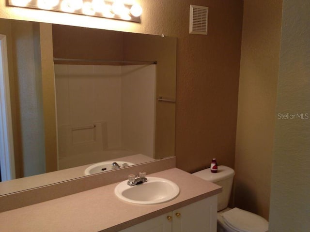 full bathroom with a textured wall, toilet, vanity, visible vents, and walk in shower