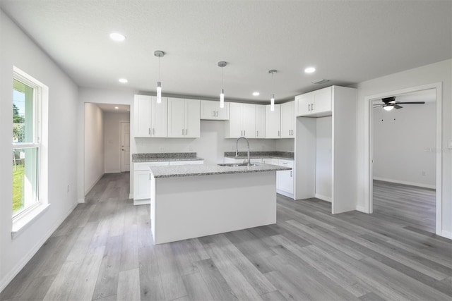 kitchen featuring light hardwood / wood-style floors, a wealth of natural light, light stone counters, and white cabinets